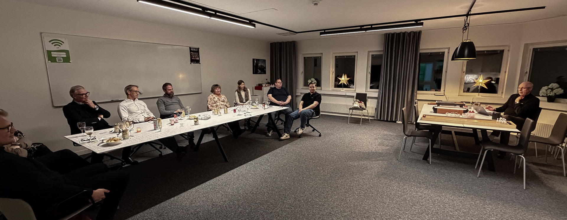 Flera personer sitter samlade runt två långbord i ett konferensrum, med mat, dryck och samtal i en ljus och modern miljö