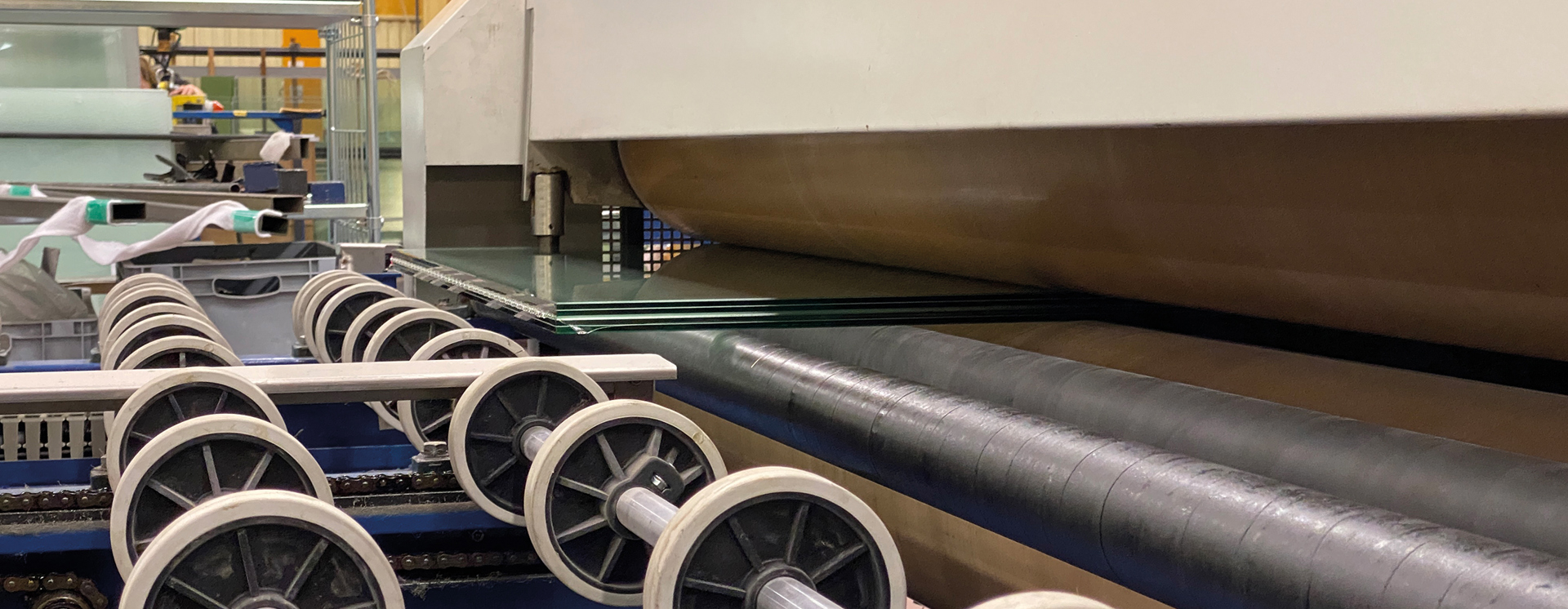 Automatiserad glasbearbetning i produktionslinje där glasrutor transporteras genom industriell maskinutrustning för tillverkning och förädling