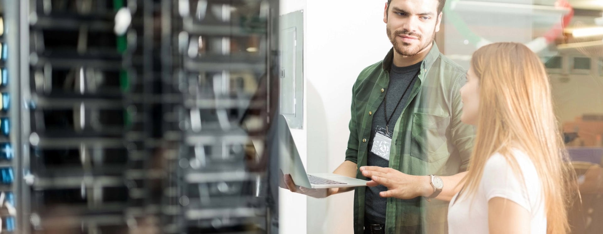 Två personer står vid serverrack i modern IT‑miljö där den ena visar information på laptop, vilket illustrerar serverdrift som tjänst, samarbete, övervakning och hantering av IT‑infrastruktur i datacenter