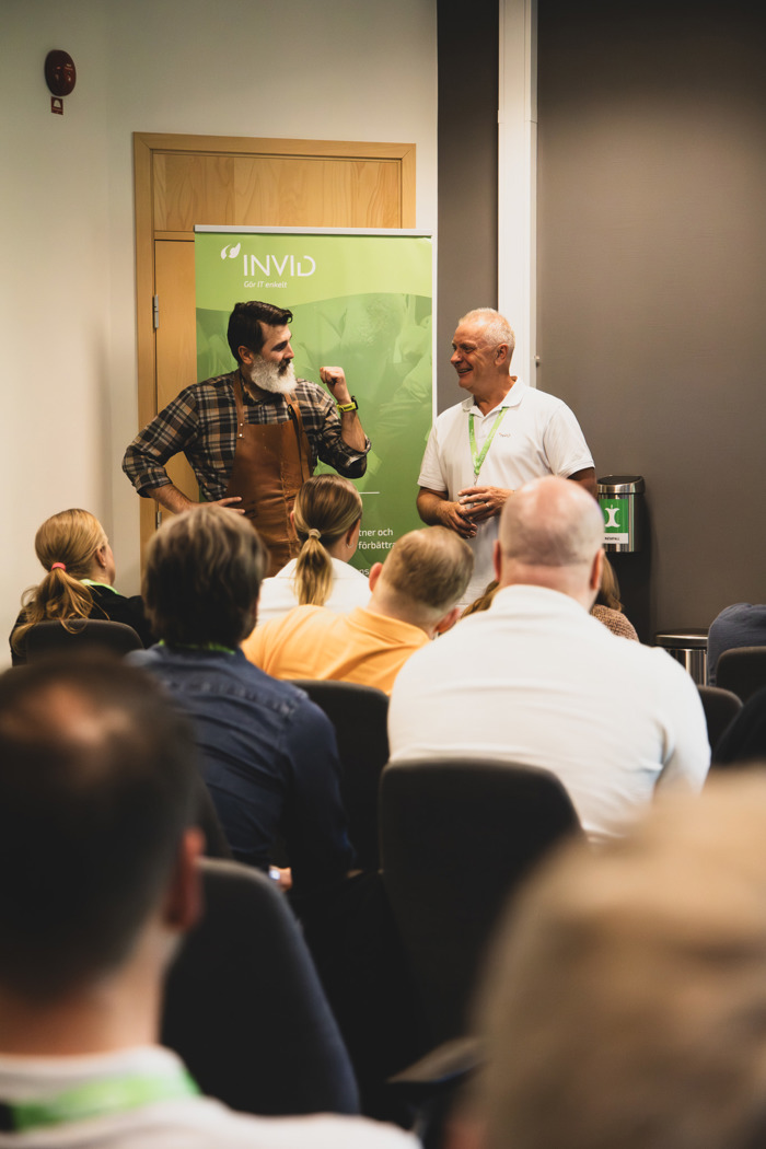 Två talare presenterar inför publik under seminarium, med INVID‑banner i bakgrunden och sittande deltagare i förgrunden.