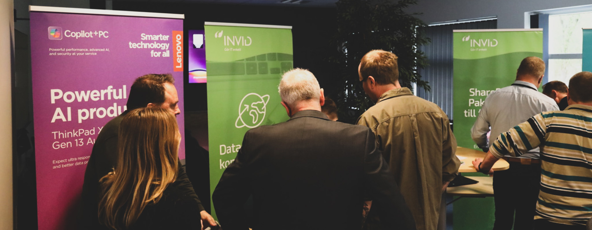 Personer nätverkar vid ståbord under event med INVID‑ och Copilot+PC‑skyltar i bakgrunden