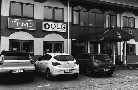 Svartvit bild på byggnad i Värnamo med bland annat skylten “INVID” på fasaden, med parkerade bilar framför