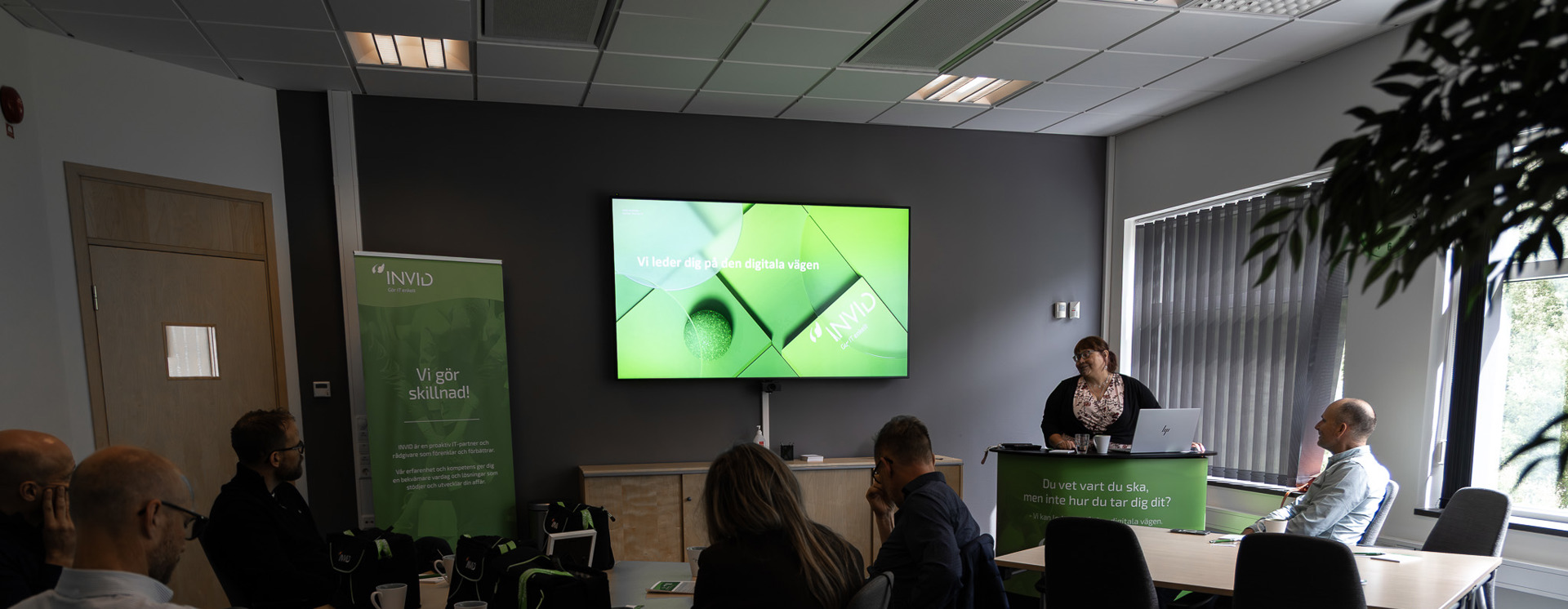 Mötesrum på INVID med presentation om digitala verktyg där deltagare sitter vid bord och lyssnar på föreläsare vid skärm