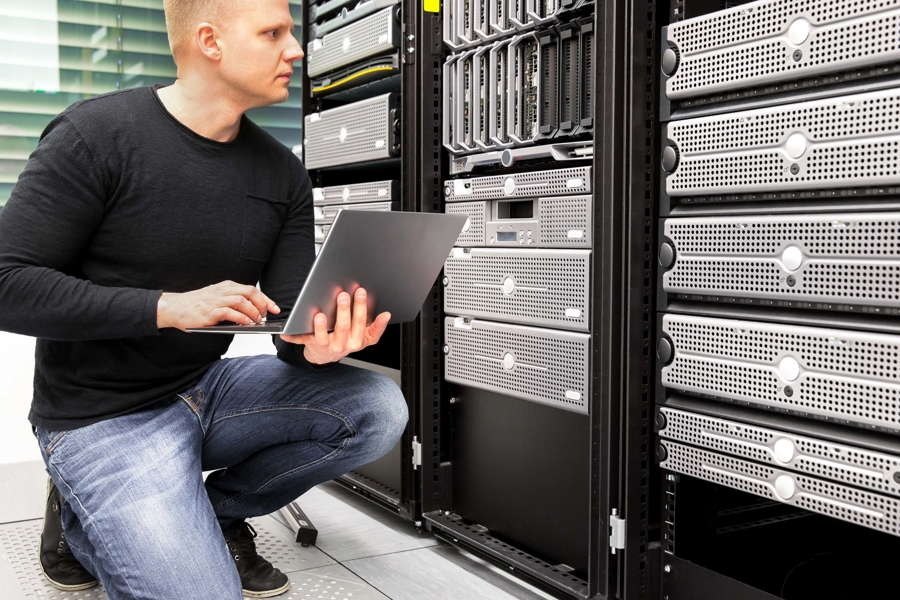 Tekniker arbetar i serverhall med laptop framför rackmonterade servrar, vilket visar övervakning, backup, drift och hantering av IT‑infrastruktur i modern datacentermiljö