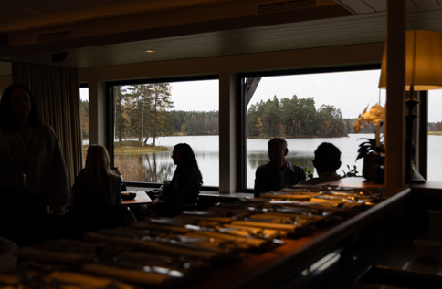 Deltagare nätverkar och samtalar i restaurangmiljö med utsikt över sjö under företagsevent, middag och affärsträff