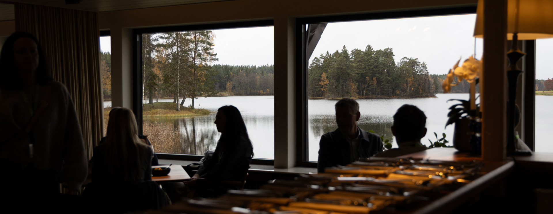 Deltagare nätverkar och samtalar i restaurangmiljö med utsikt över sjö under företagsevent, middag och affärsträff