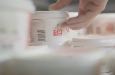 Hand plockar SIA Glass-förpackning från produktionslinje i livsmedelsindustri med fokus på kvalitetssäkring och förpackningshantering