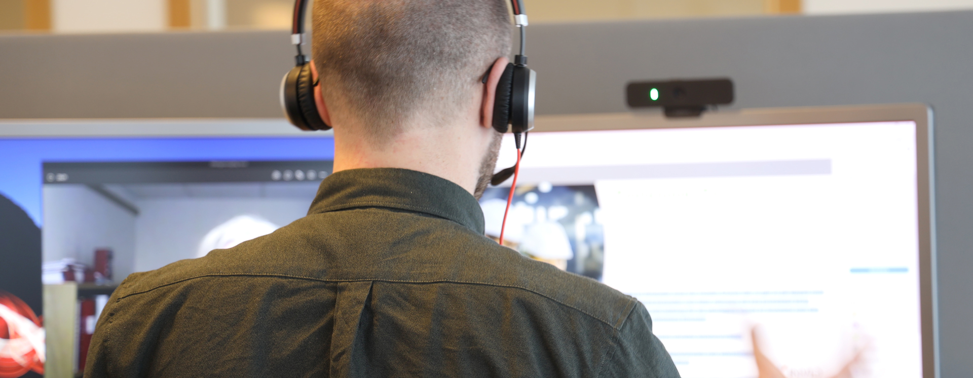 Person med headset arbetar vid flera datorskärmar och interagerar med digitalt gränssnitt i modern IT- och kontorsmiljö