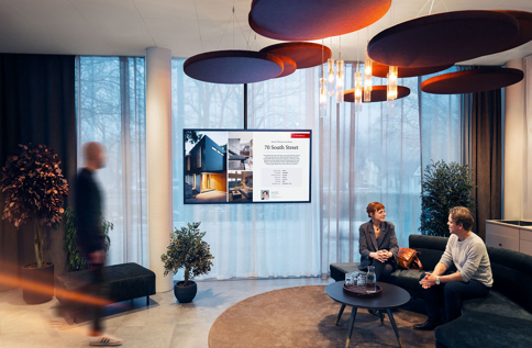 Digital informationsskärm i modern lobby visar fastighetsinformation och innehåll via Smartsign, medan besökare vistas i gemensam lounge- och receptionsmiljö