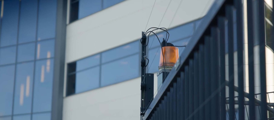 Staket med monterad orange varningslampa framför en modern byggnad med glasfasad
