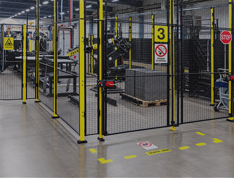 Säkerhetsinhägnad med gula stolpar och nätpaneler runt en maskinavdelning i en modern fabrik