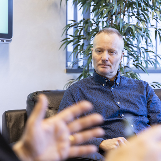 Person sitter i en soffa i ett kontor och samtalar med en annan person utanför bild, med en grön växt i bakgrunden
