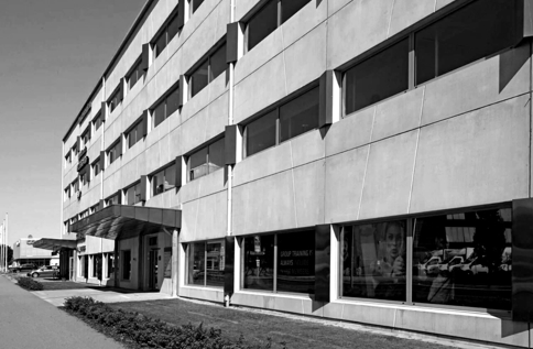 Svartvit bild på INVIDs kontor i Halmstad i modern kontorsfastighet med stora fönster och entré längs gatan