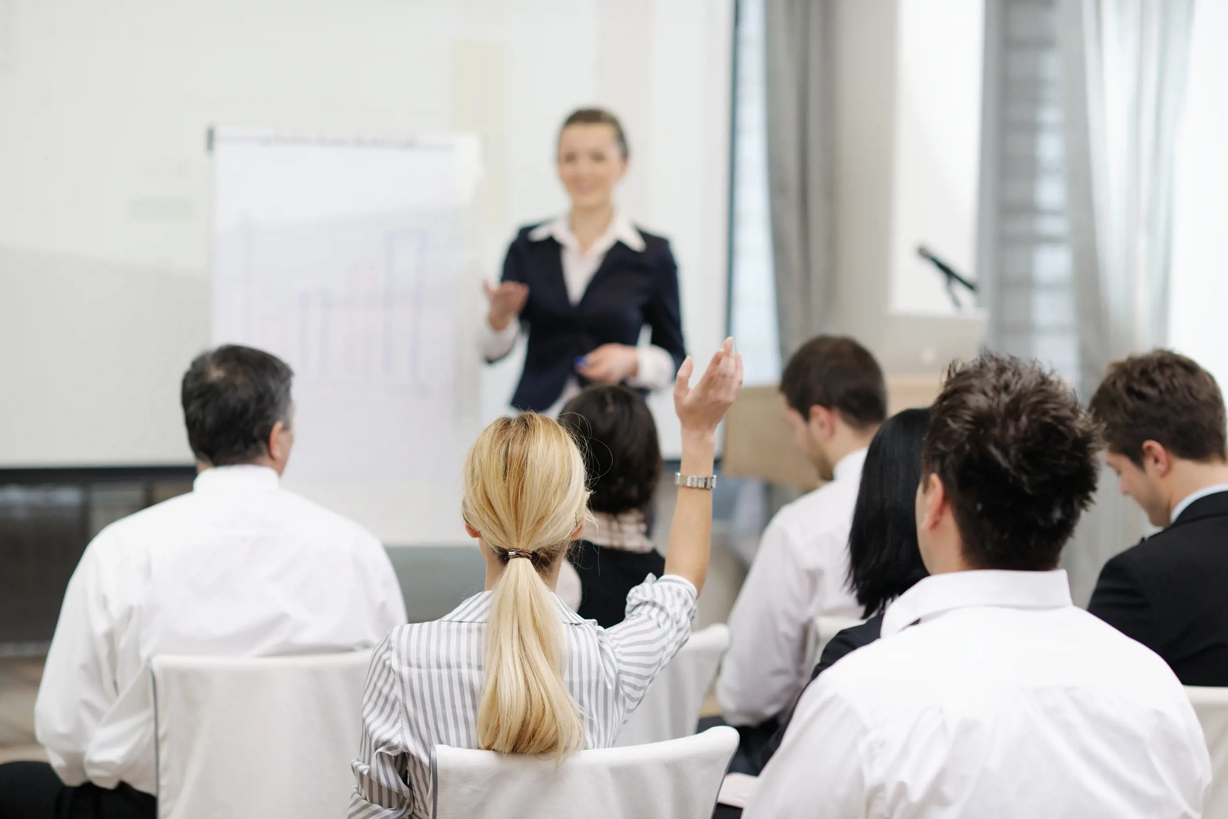 Grupp personer deltar i en utbildning där en föreläsare presenterar vid whiteboard, medan en deltagare räcker upp handen, vilket illustrerar användarutbildning och ökad medvetenhet kring IT‑säkerhet