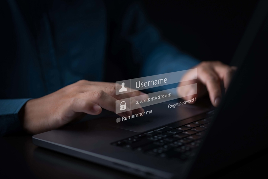 Närbild av händer som skriver på laptop med inloggningsruta och lösenordsfält på skärm, vilket illustrerar IT‑säkerhet, autentisering och skydd av system genom brandvägg och säker inloggning