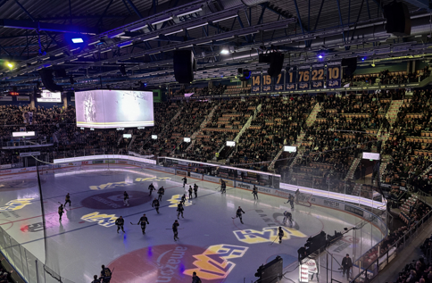Hockeymatch i fullsatt arena med spelare på isen, storbildsskärm, publik på läktarna och exponering av INVID:s varumärke