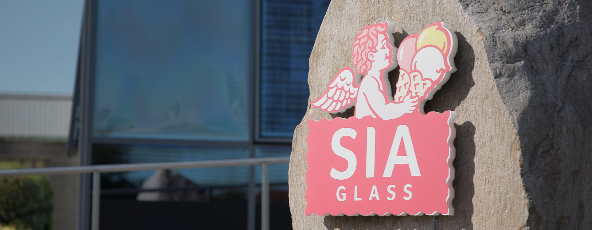 SIA Glass-logotyp monterad på natursten utanför företagsbyggnad med glasfasad, som symboliserar varumärke och verksamhet