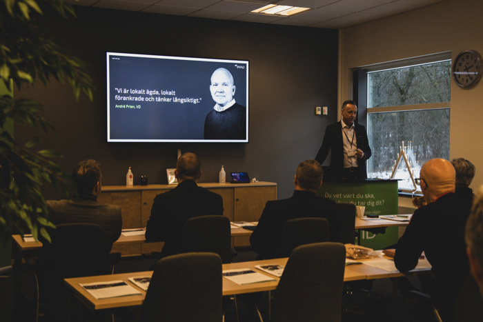 Seminarium i ett konferensrum där en Richard Wahlstedt presenterar vid en skärm, medan deltagare sitter vid bord med anteckningar och laptop, och en INVID‑skylt står vid sidan