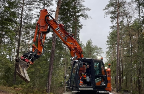 Bandgrävare arbetar med mark- och anläggningsarbete i skogsmiljö där väg eller infrastruktur byggs med hjälp av tung entreprenadutrustning