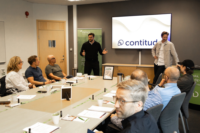 Presentatör håller genomgång vid konferensbord med skärm i bakgrunden