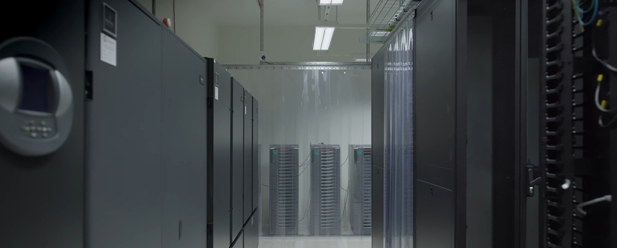 Serverrum med långa rader av serverrack i en ljus och ren miljö, med teknikskåp på båda sidor och utrustning synlig längre in i rummet