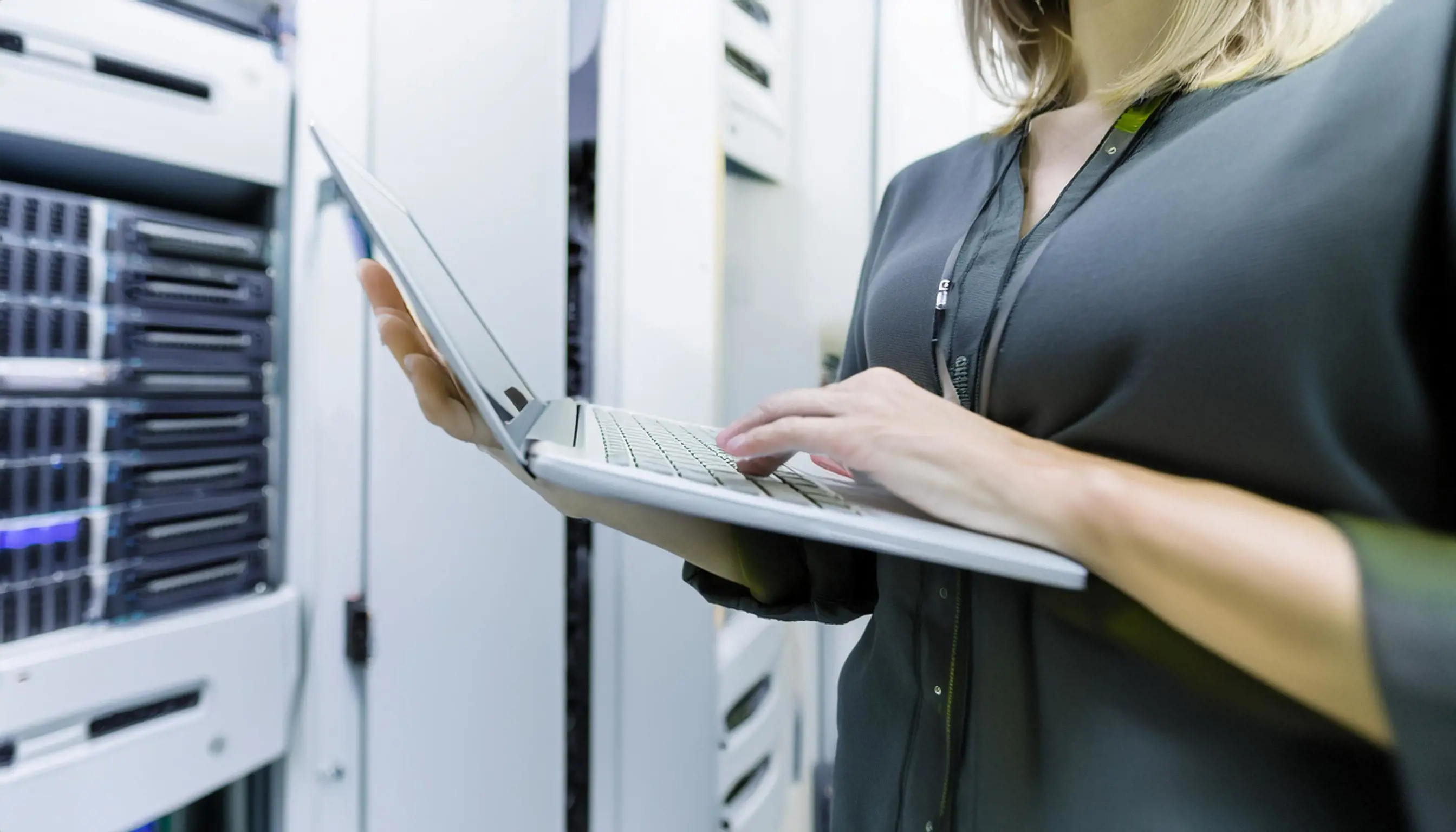 Närbild på en person som använder en laptop i ett serverrum med öppna rackskåp i bakgrunden, vilket symboliserar arbete med både serversäkerhet och klientsäkerhet
