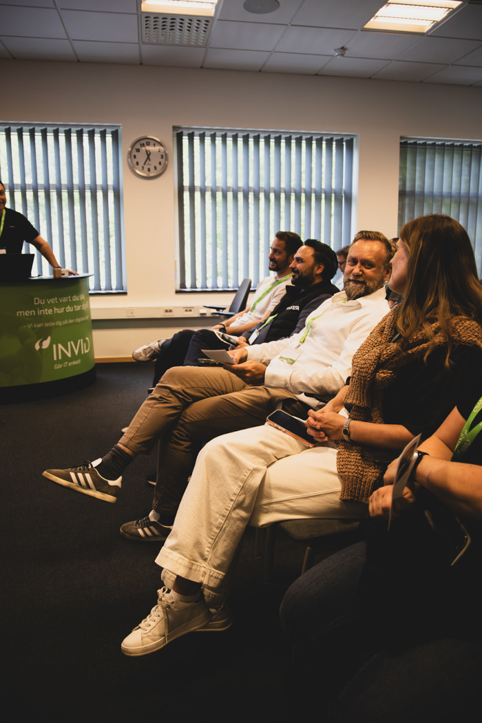 Deltagare sitter i publik under event medan en man i förgrunden, som kom trea i tävlingen, tittar mot scenen där presentation pågår.
