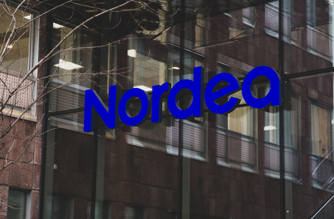 Entré med glasfasad där den blå Nordea-logotypen syns på byggnaden, med reflektioner av omgivande hus i glaset
