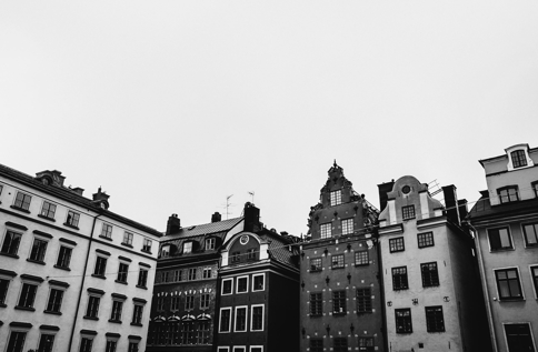 Svartvit Bild På Äldre Byggnader Med Olika Fasader Och Taklinjer Står På Rad Under En Grå Himmel, Med Tydliga Detaljer Som Fönster Och Dekorationer