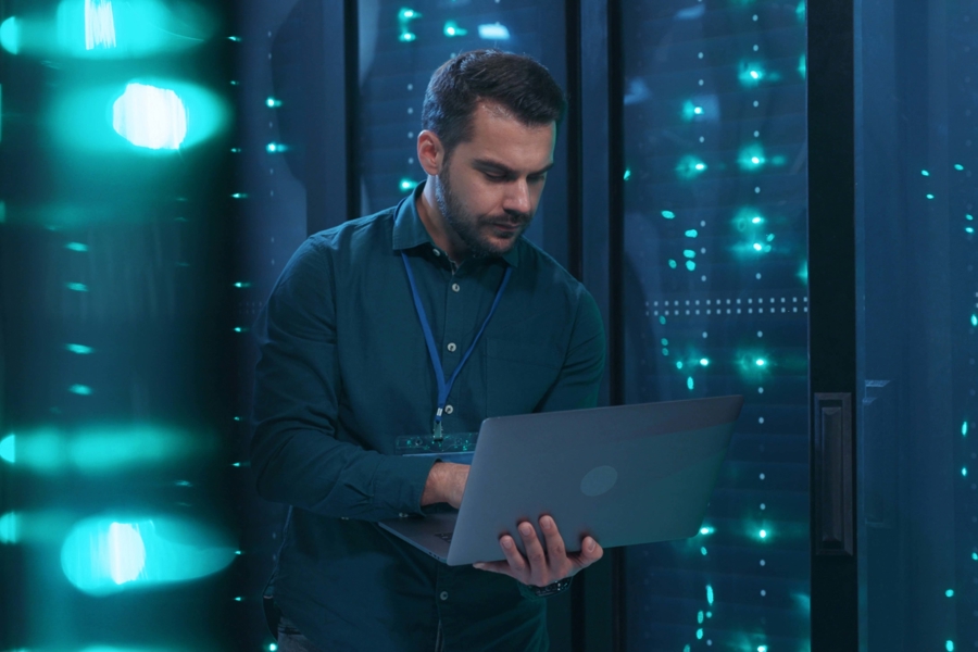 Person arbetar med en laptop i ett serverrum, omgiven av serverrack med lysande indikatorer