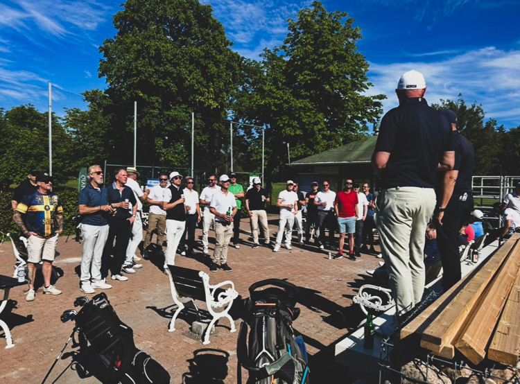 Deltagare samlade för information och vid golfevent utomhus med golfbagar och klubbhus i bakgrunden