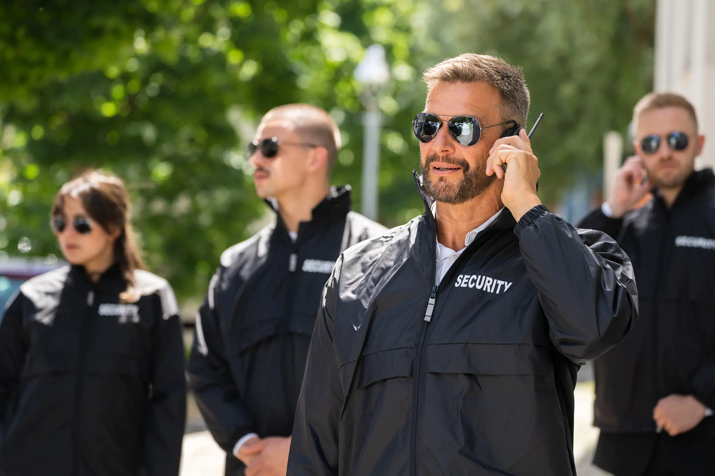 Säkerhetspersonal i uniform med texten “Security” som kommunicerar via radio i en utomhusmiljö, vilket illustrerar samordning och red teaming