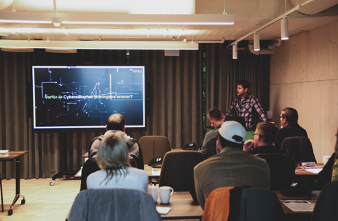 Robin Rosengren presenterar om cybersäkerhet inför sittande publik med projektorskärm och presentation i konferensrum