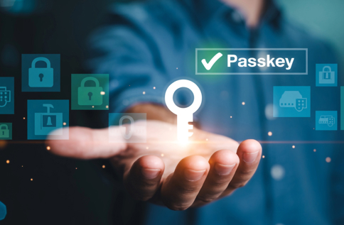 Hand håller upp en digital nyckelsymbol med texten “Passkey”, omgiven av ikoner för lås, autentisering och säkerhet mot en blåtonad bakgrund