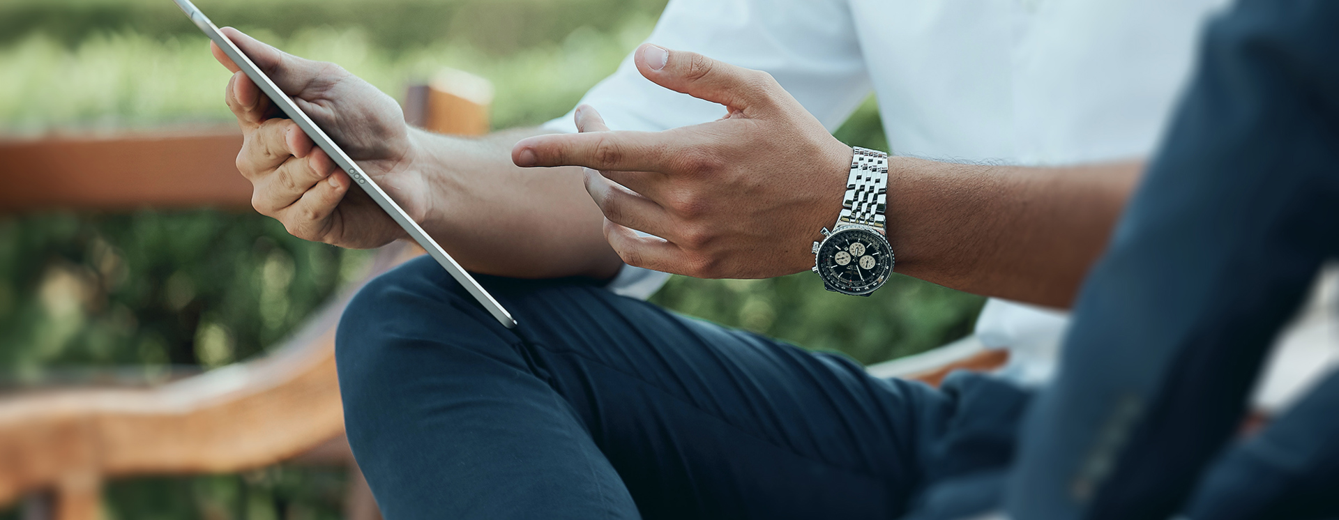 Närbild på två personer som sitter utomhus, där en håller en surfplatta och pekar på skärmen och den andra sitter bredvid