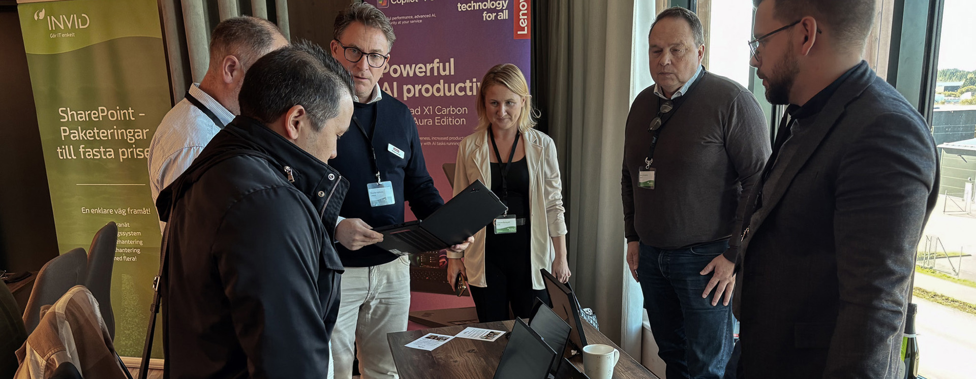 Flera deltagare studerar laptops vid demo, med Lenovo Copilot+ PC‑banner och SharePoint‑rollup i konferensmiljö
